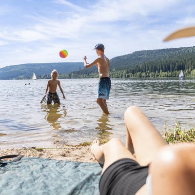 Urlauber spielen am sonnigen Ufer des Schluchsees im Schwarzwald mit einem Wasserball.