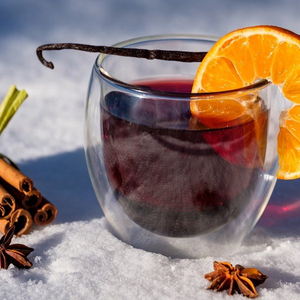 Ein Glas heißer Glühwein mit einer Orangenscheibe und Zimtstangen im Schnee.