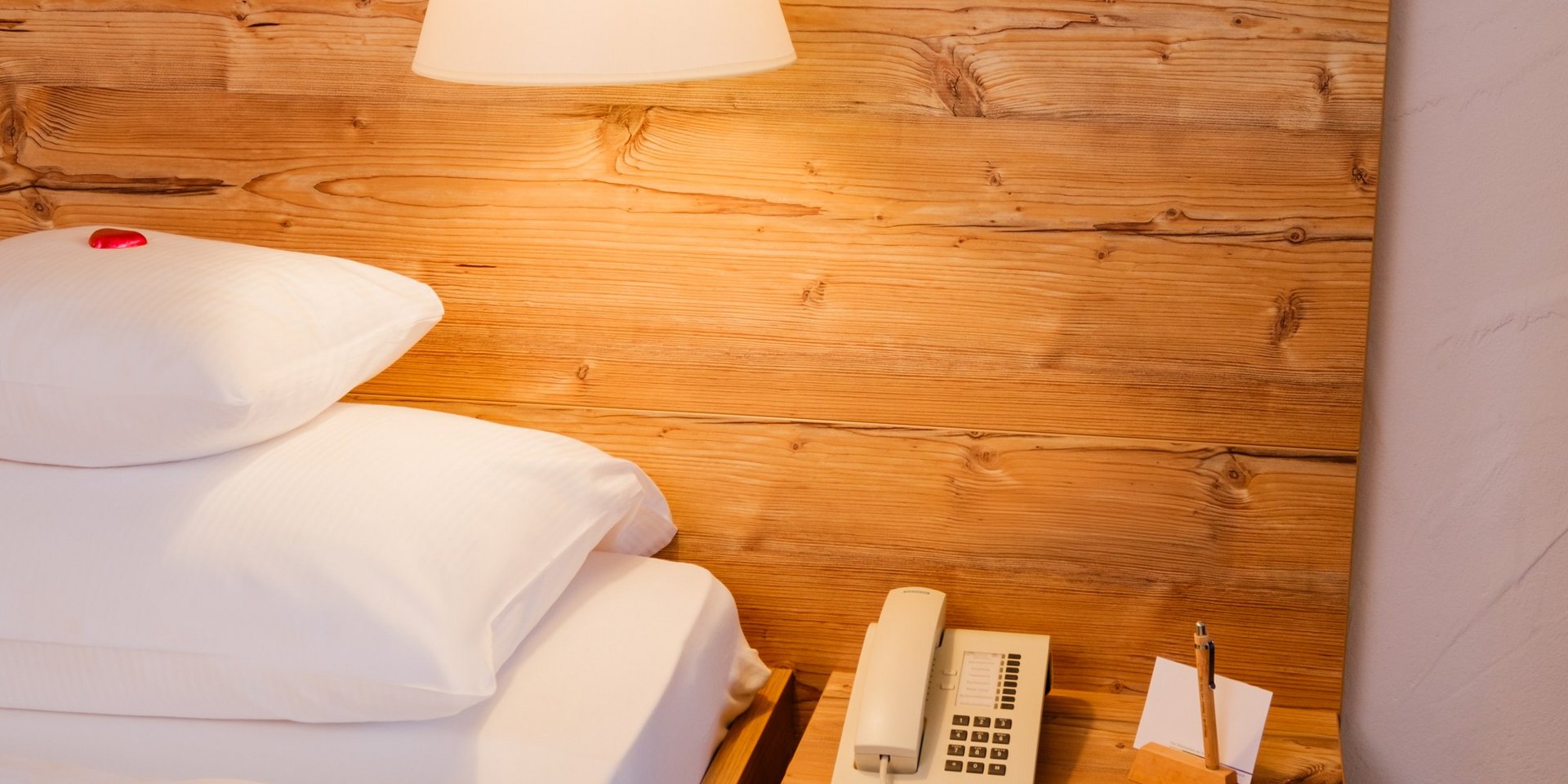 Detailansicht des gemütlichen Betts mit Holzelementen und Nachttischlampe im Hotel Vier Jahreszeiten am Schluchsee.