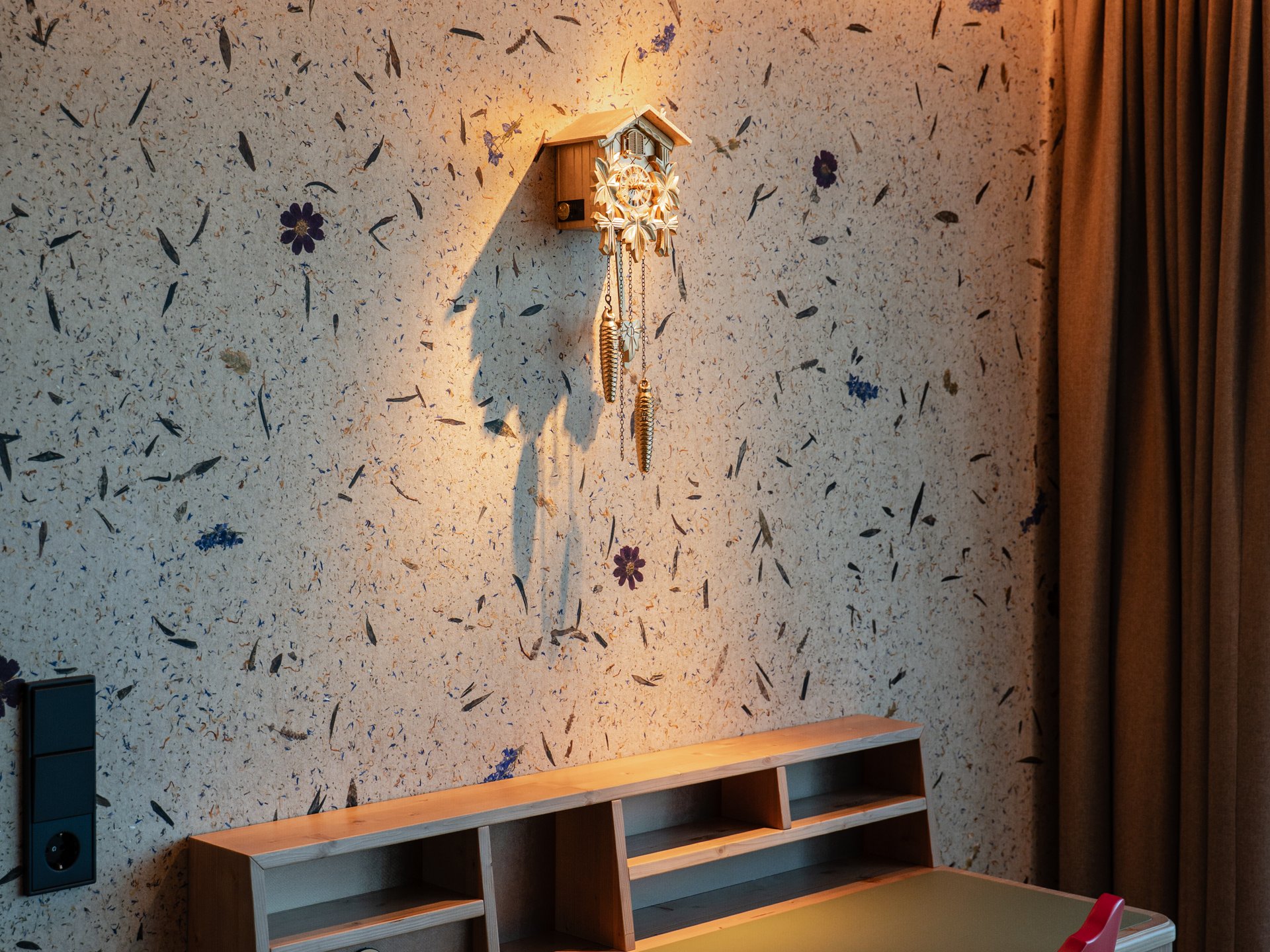 Schreibtisch mit Kuckucksuhr an der Wand mit Wiesentapete im Hintergrund