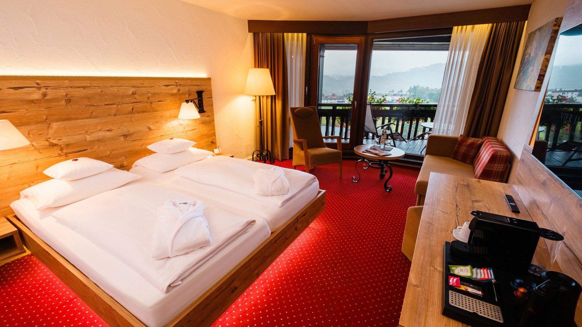 Helles Doppelzimmer mit komfortablem Doppelbett, rotem Teppichboden und Holzverkleidung im Hotel Vier Jahreszeiten.