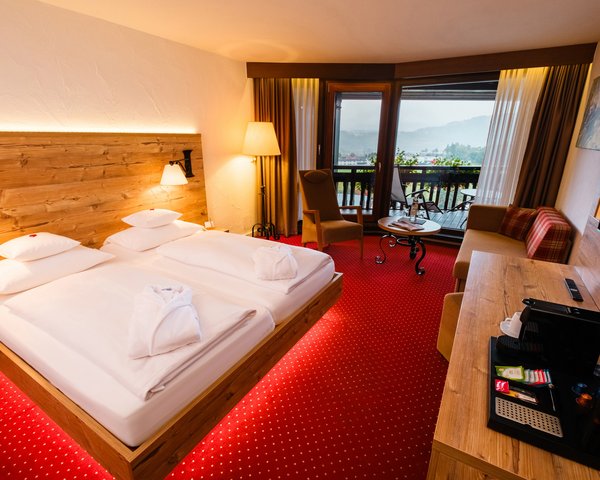 Helles Doppelzimmer mit komfortablem Doppelbett, rotem Teppichboden und Holzverkleidung im Hotel Vier Jahreszeiten.