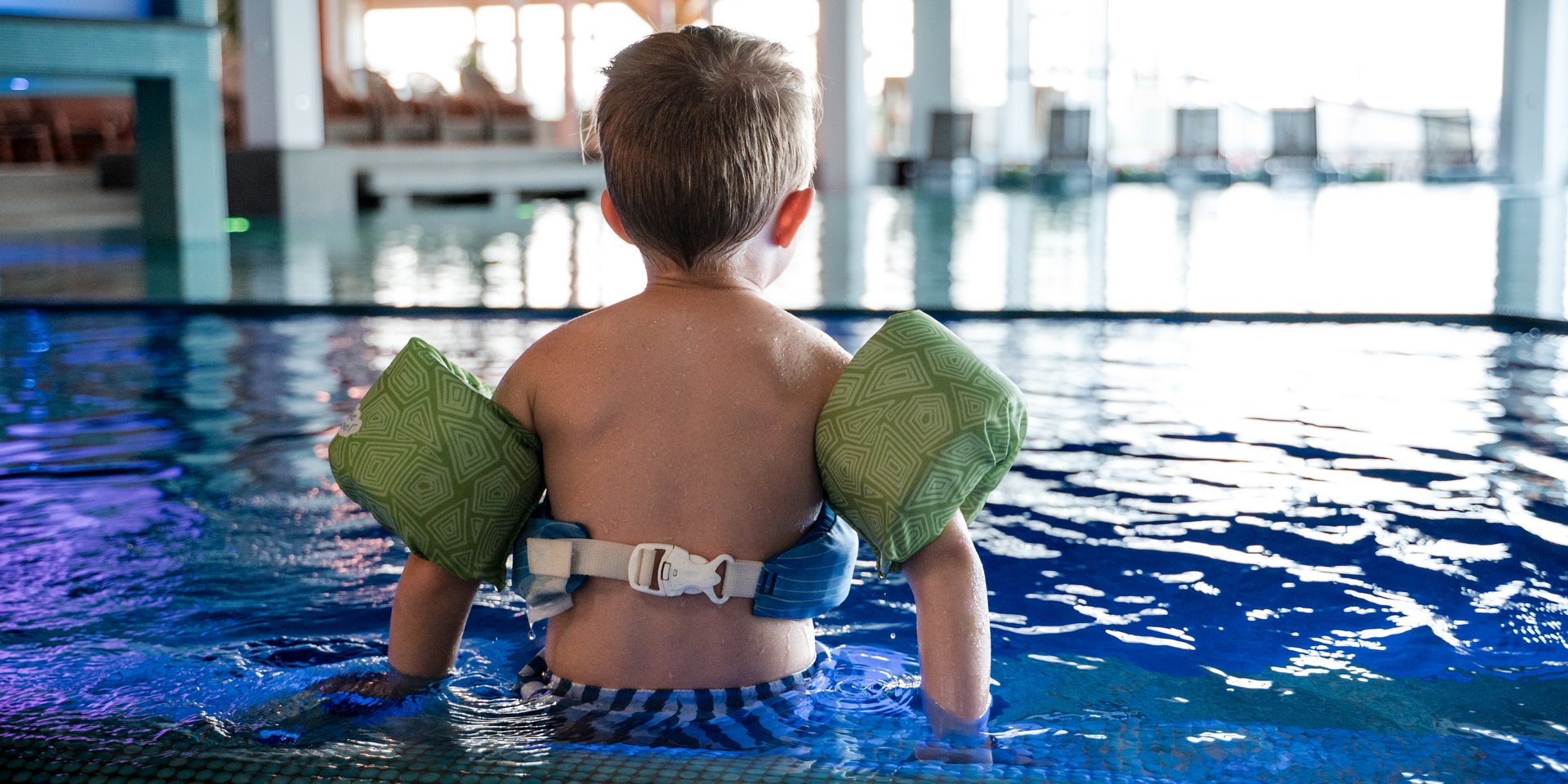 Junge sitzt mit Schwimmflügeln am Rand des Pools