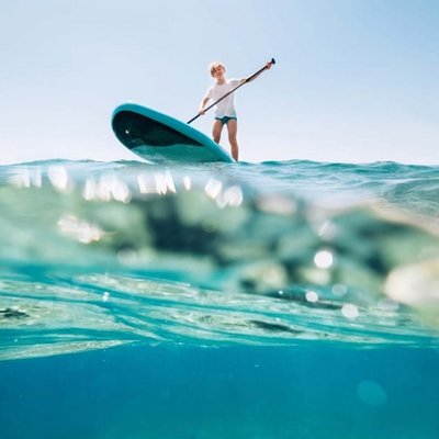 Eine Person balanciert auf einem SUP-Board inmitten des klaren Wassers.