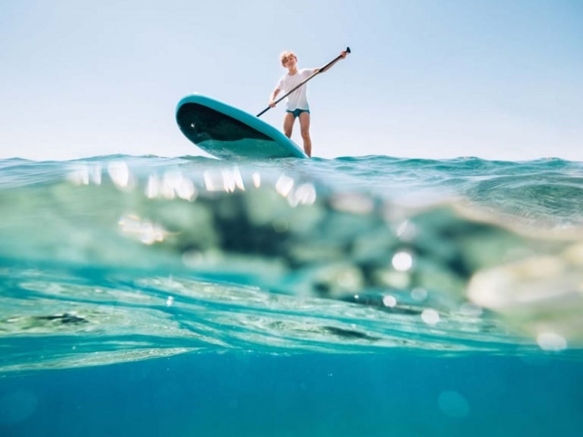 Eine Person balanciert auf einem SUP-Board inmitten des klaren Wassers.