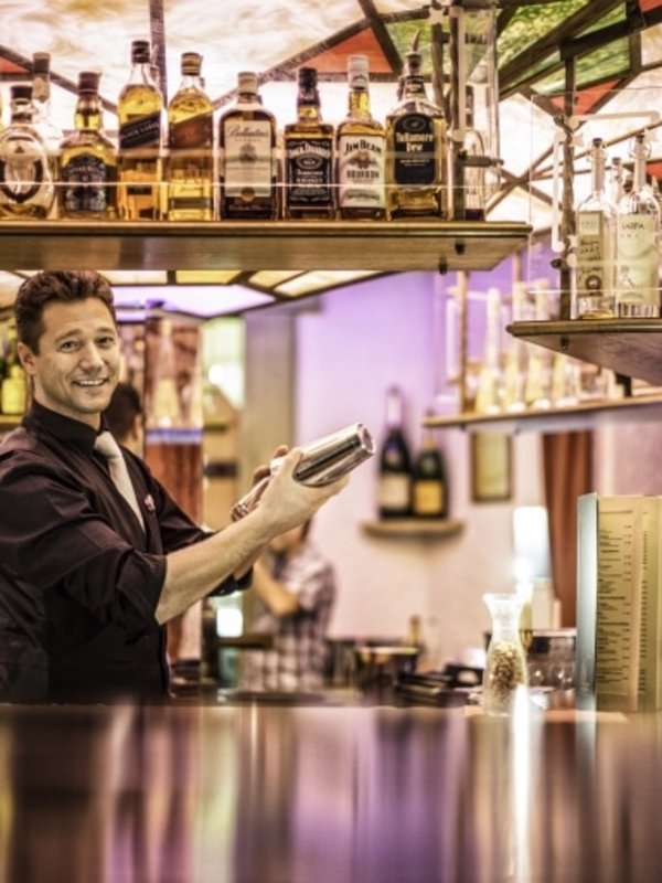 Ein Barkeeper bereitet fachmännisch Cocktails an der ikonischen Karussellbar des Hotels Vier Jahreszeiten vor.