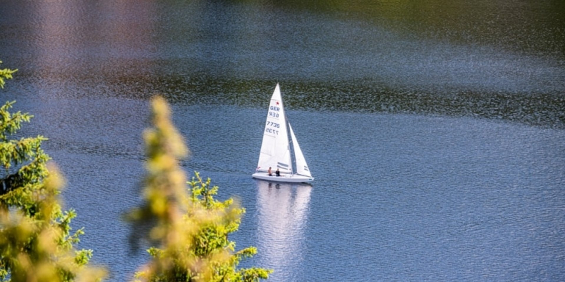 Ein weißes Segelboot gleitet bei ruhigem Wetter über den tiefblauen Schluchsee im Schwarzwald.