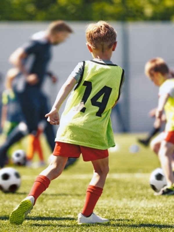 Kinder spielen gemeinsam Fußball auf einem Sportplatz während eines aktiven Urlaubstages.