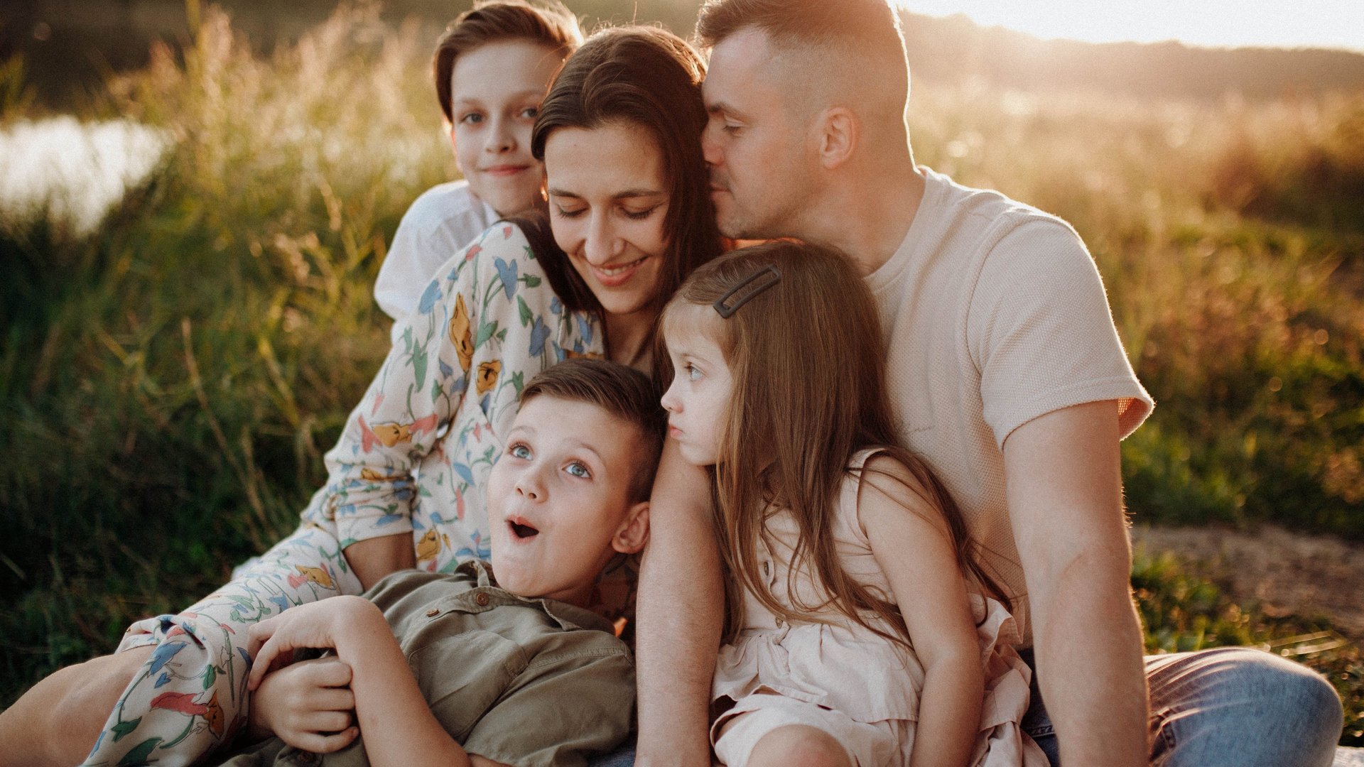 Familie mit Mutter, Vater, und 3 Kindern sitzen am See 