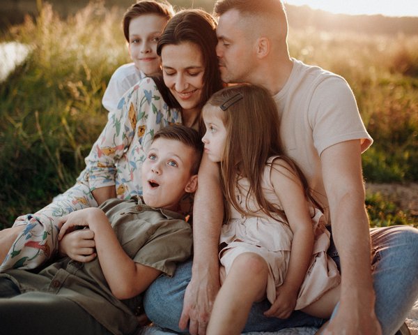 Familie mit Mutter, Vater, und 3 Kindern sitzen am See 