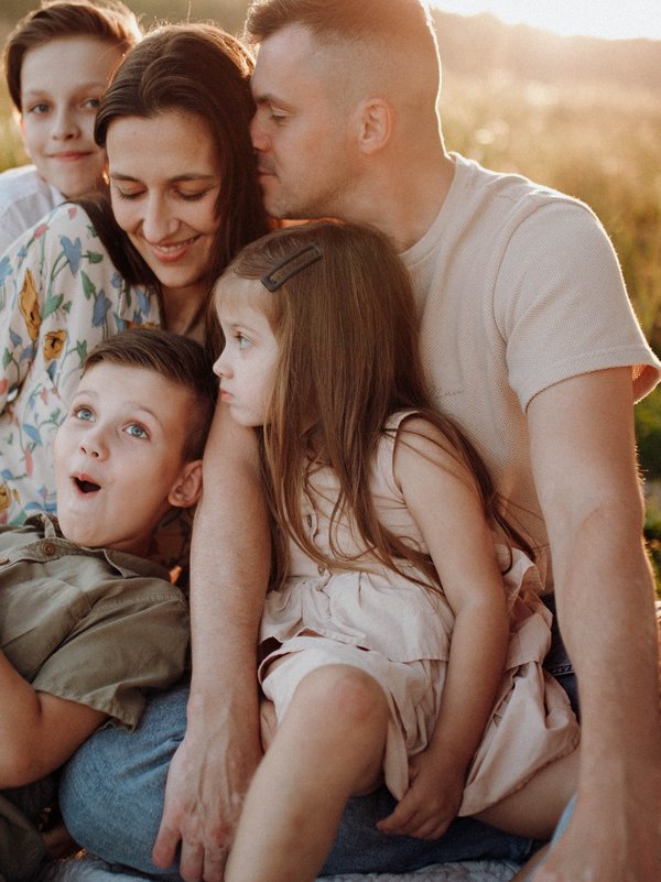Familie mit Mutter, Vater, und 3 Kindern sitzen am See 