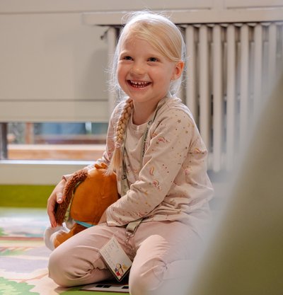 Ein kleines Mädchen sitzt vergnügt in der hellen Spielecke des Hotels Vier Jahreszeiten im Schwarzwald.