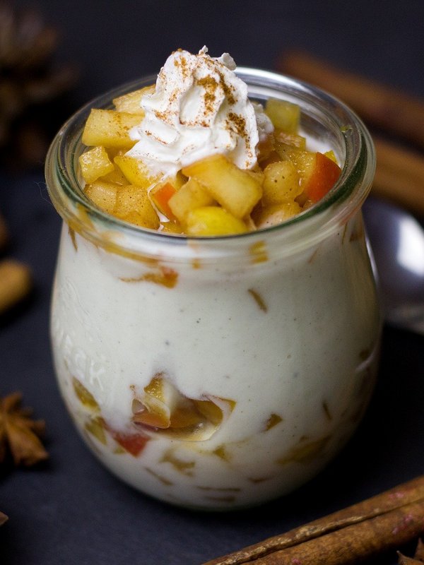 Ein appetitlich angerichtetes Schichtdessert im Glas mit Sahnehaube und Zimtstangen als Dekoration.