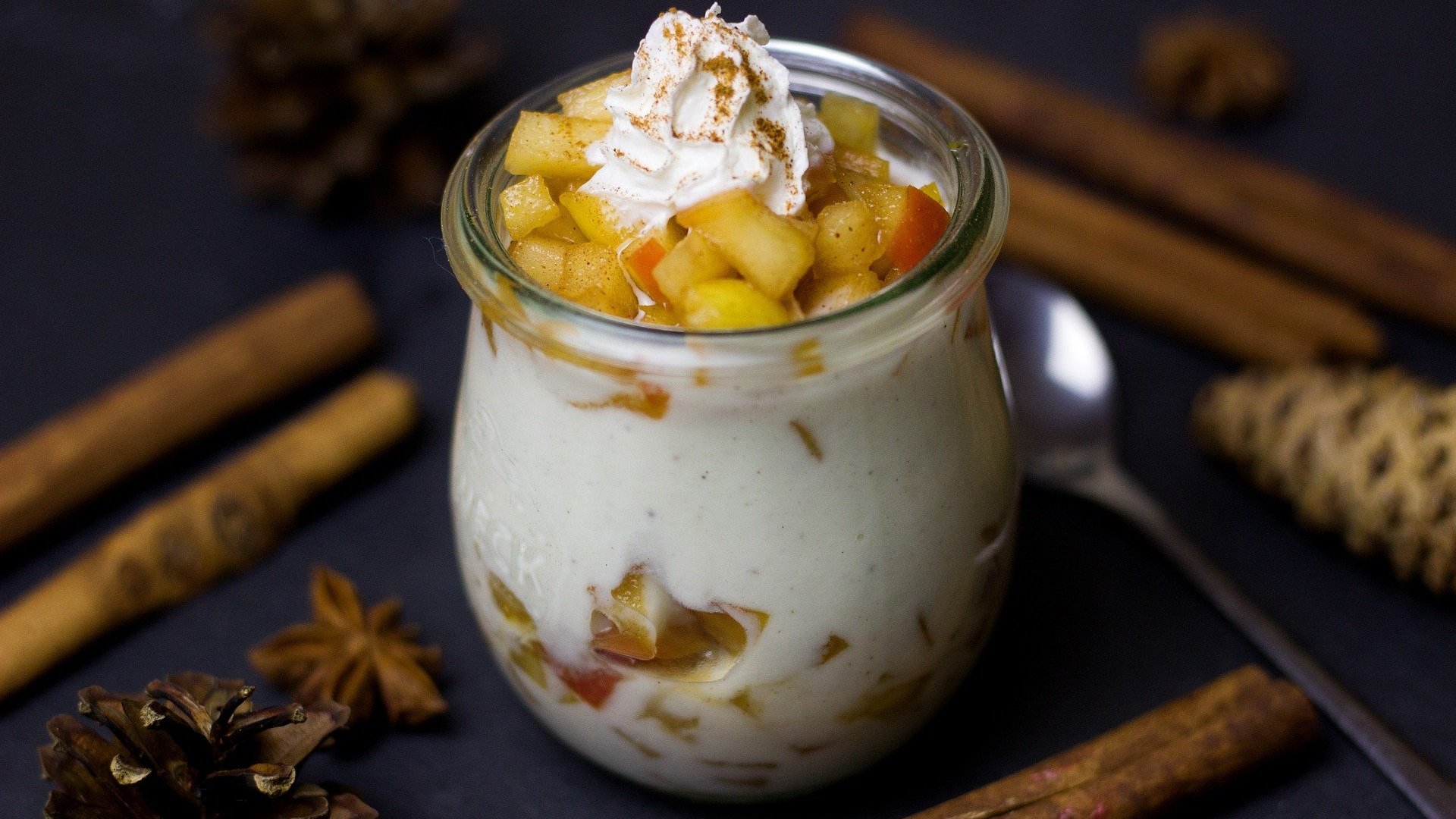 Ein appetitlich angerichtetes Schichtdessert im Glas mit Sahnehaube und Zimtstangen als Dekoration.