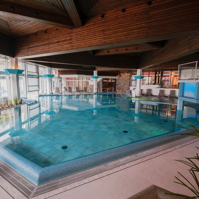 Großzügiges Hallenbad mit moderner Beleuchtung und Blick auf die hölzerne Deckenkonstruktion im Hotel Vier Jahreszeiten am Schluchsee.