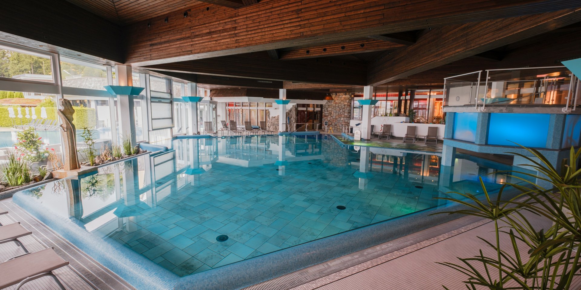 Großzügiges Hallenbad mit moderner Beleuchtung und Blick auf die hölzerne Deckenkonstruktion im Hotel Vier Jahreszeiten am Schluchsee.