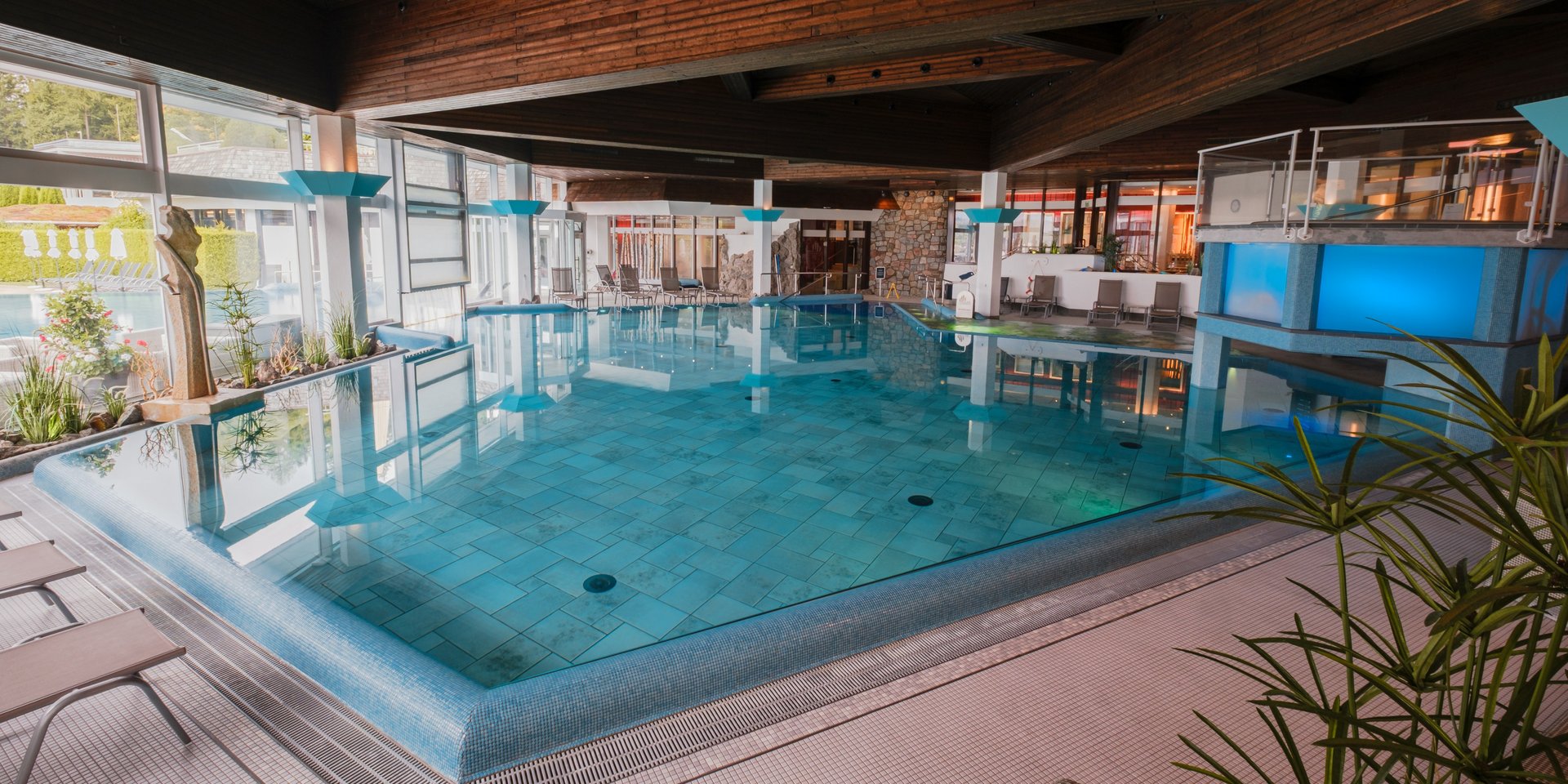 Großzügiges Hallenbad mit moderner Beleuchtung und Blick auf die hölzerne Deckenkonstruktion im Hotel Vier Jahreszeiten am Schluchsee.