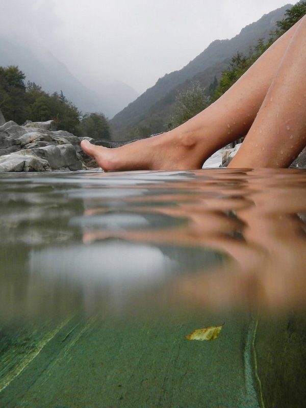 Detailansicht von Füßen, die zur Erfrischung nach einer Wanderung in das klare Wasser eines Bergbachs tauchen.