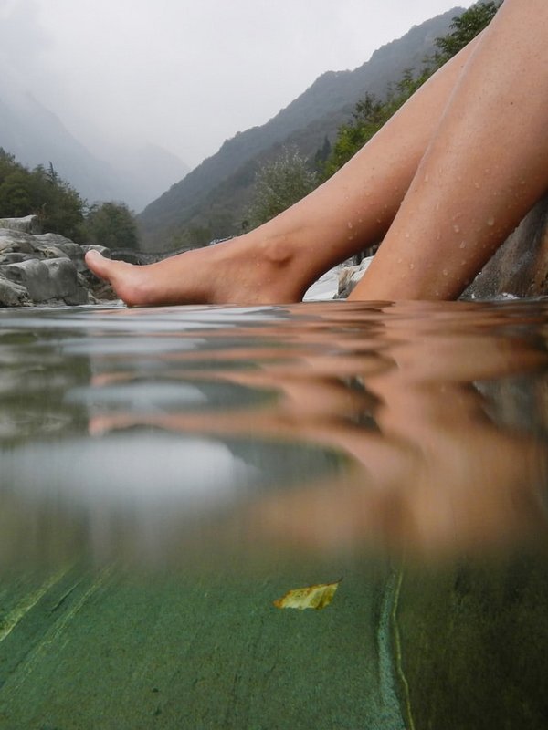 Detailansicht von Füßen, die zur Erfrischung nach einer Wanderung in das klare Wasser eines Bergbachs tauchen.