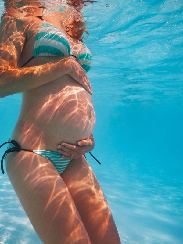Unterwasseraufnahme einer schwangeren Frau beim ruhigen Schwimmen im Pool.