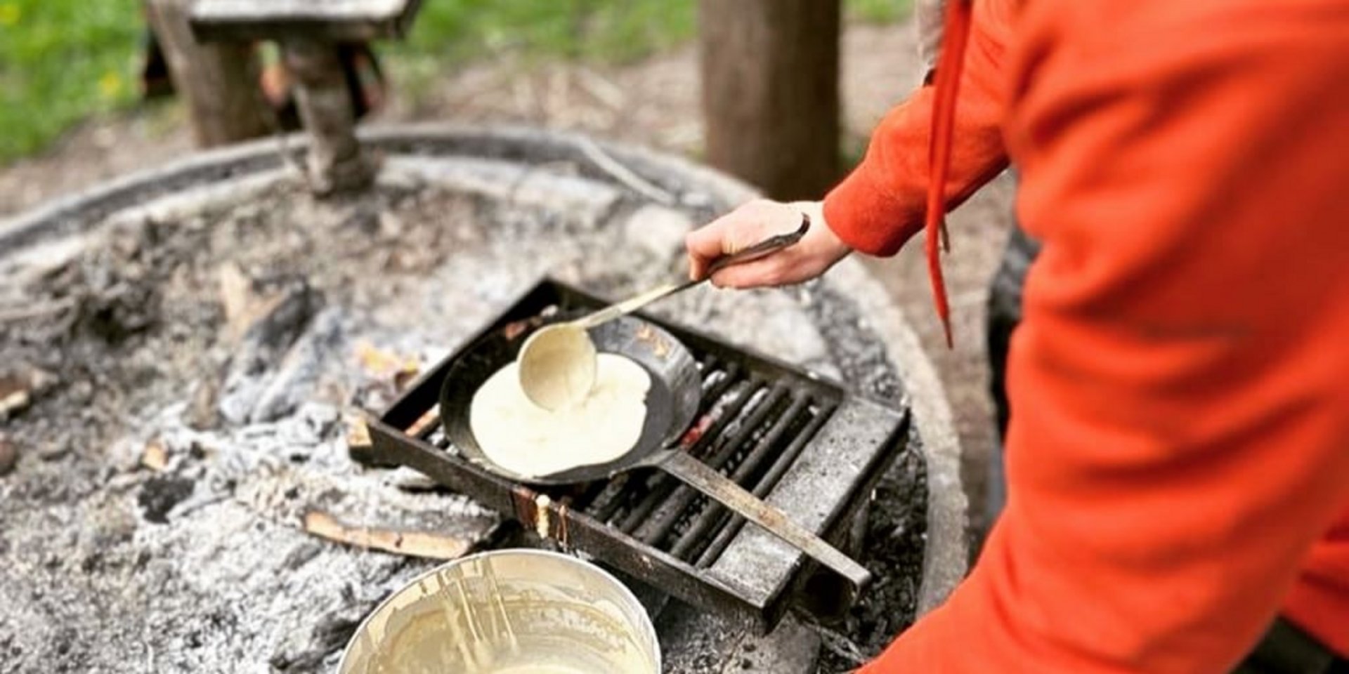 Ein Teilnehmer bereitet über einem offenen Feuer eine Mahlzeit während eines Wildnis-Workshops zu.