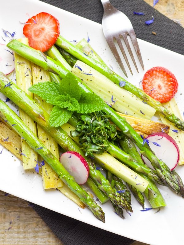Ein Teller mit frisch zubereitetem grünen Spargel, Kirschtomaten und feinen Kräutern.