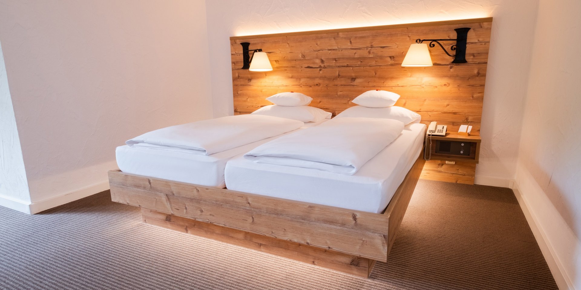 Komfortables Doppelbett mit indirekter Beleuchtung und rustikaler Holzwand im Hotel Vier Jahreszeiten am Schluchsee.