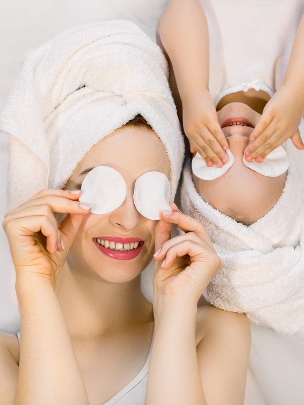 Mutter und Kind entspannen gemeinsam mit Watteaus auf den Augen während eines Wellnesstages.