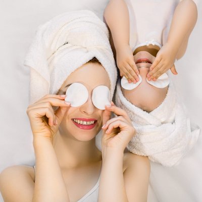 Mutter und Kind entspannen gemeinsam mit Watteaus auf den Augen während eines Wellnesstages.