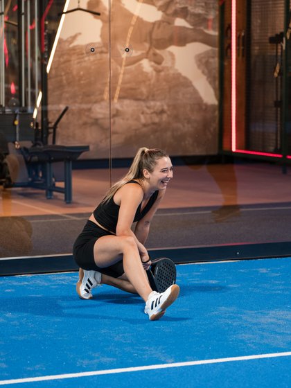 Eine Frau führt Dehnübungen auf dem blauen Sportboden der hoteleigenen Halle aus.