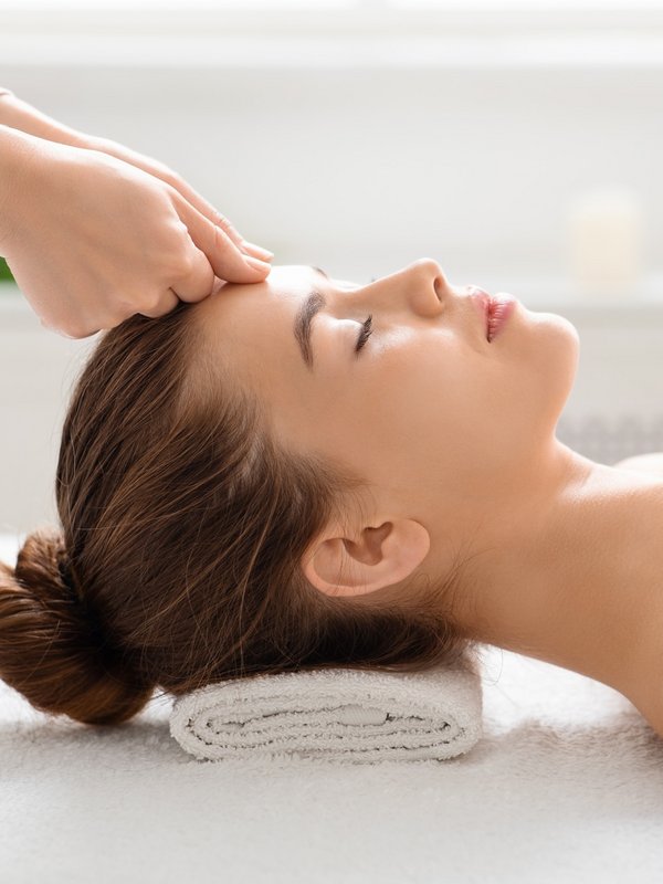 Sanfte Streichbewegungen an der Stirn einer Frau während einer professionellen Gesichtsbehandlung.