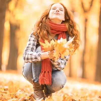 Ein Kind wirft im herbstlichen Wald freudig eine Handvoll bunter Blätter in die Luft.
