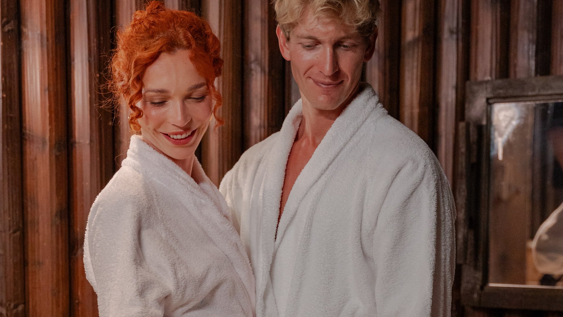 Ein Paar in weißen Bademänteln steht lächelnd vor einer großen Kupferwanne im Kaiserbad des Hotels Vier Jahreszeiten am Schluchsee.