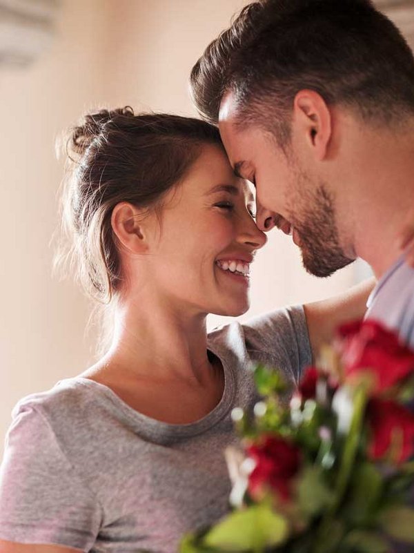 Ein Paar steht sich eng gegenüber; der Mann hält einen Strauß roter Rosen.