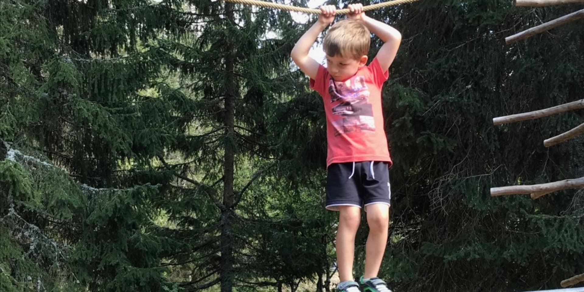Ein Mädchen testet seine Geschicklichkeit an einem Seil-Parcours im Wald.