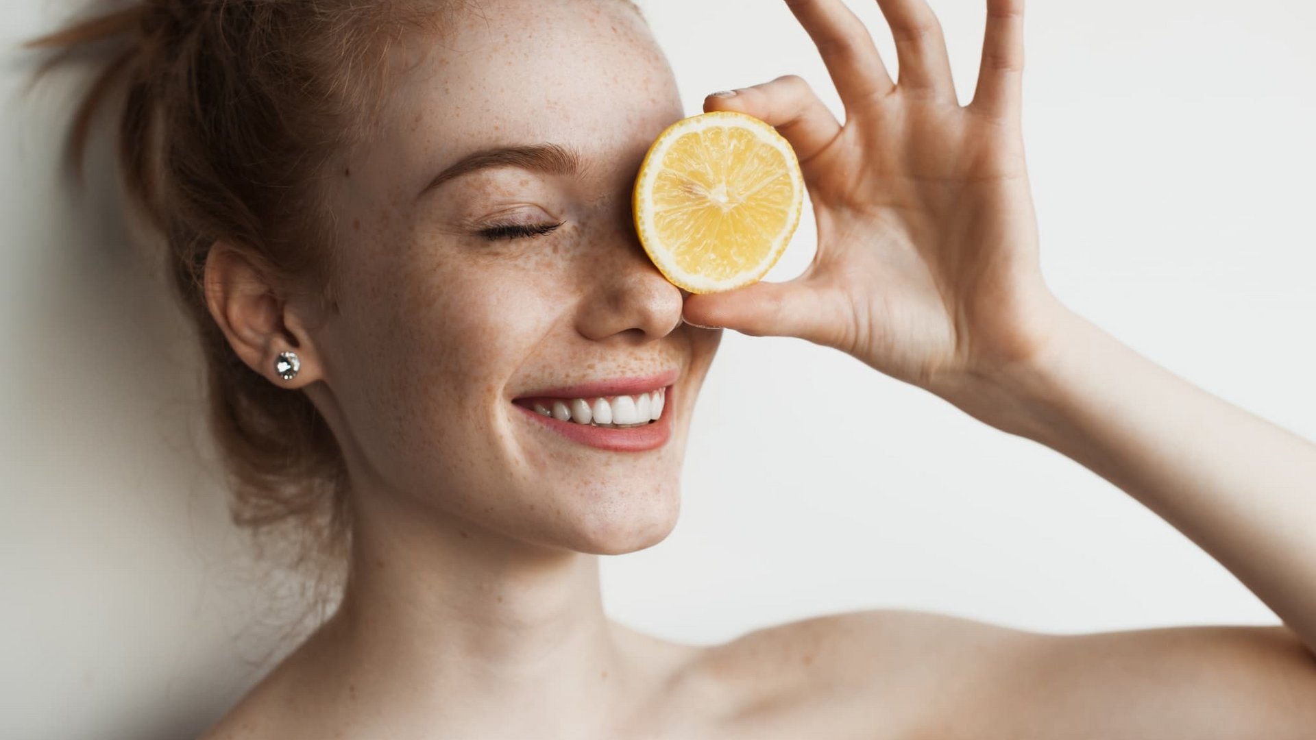 Porträt einer lachenden Frau, die sich eine Zitronenscheibe vor das Auge hält.