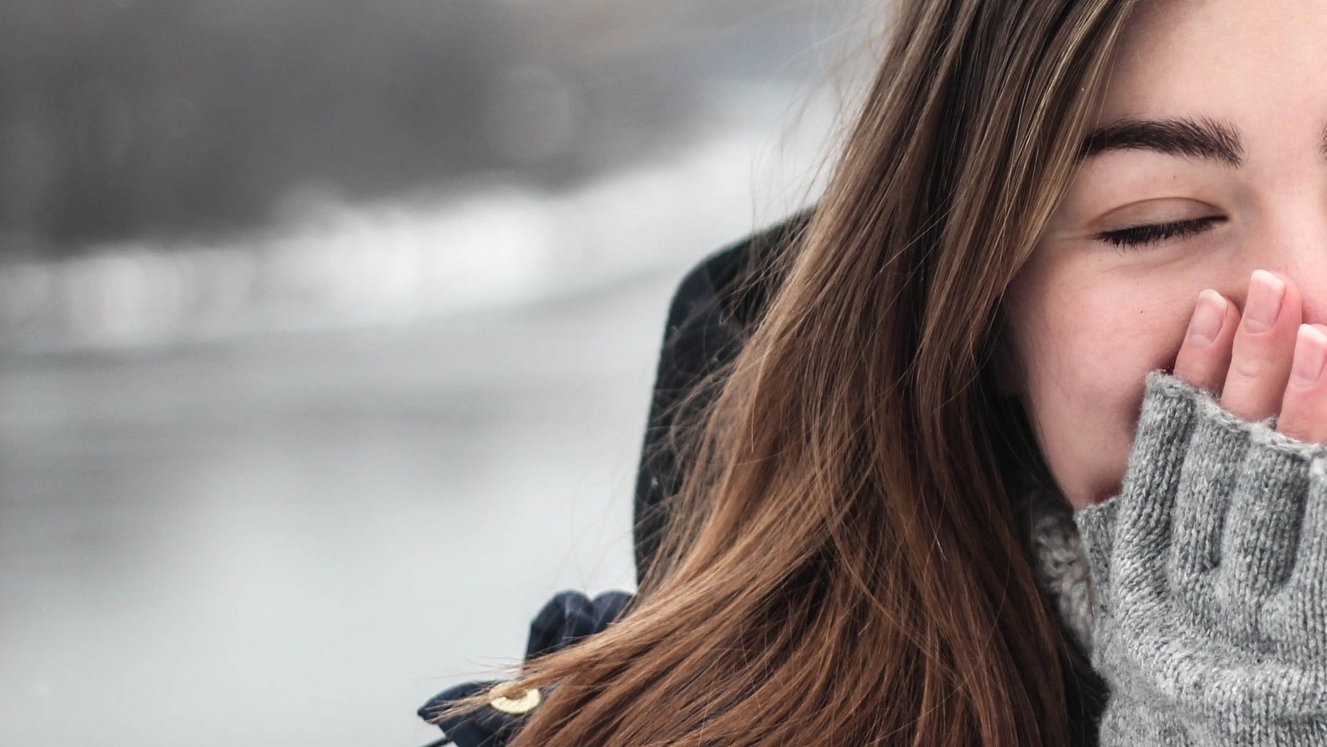 Eine junge Frau in warmer Winterkleidung lächelt in einer verschneiten Landschaft.