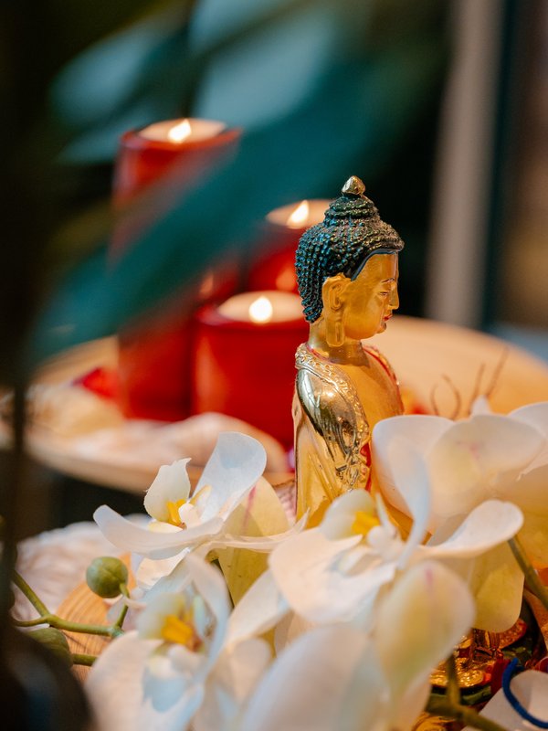 Eine kleine Buddha-Statue umgeben von brennenden roten Kerzen und weißen Orchideenblüten im Hotel Vier Jahreszeiten am Schluchsee.