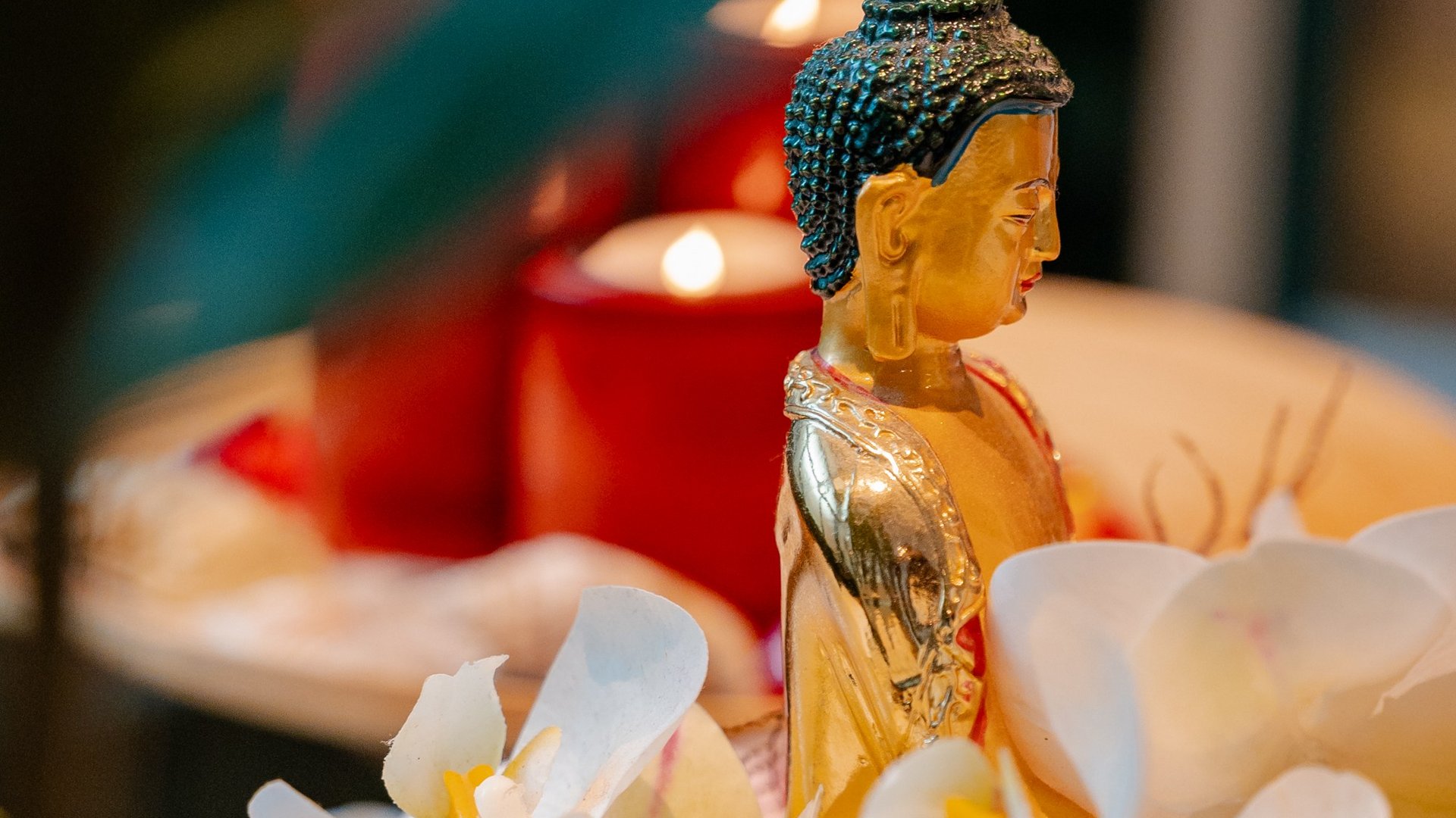 Eine kleine Buddha-Statue umgeben von brennenden roten Kerzen und weißen Orchideenblüten im Hotel Vier Jahreszeiten am Schluchsee.