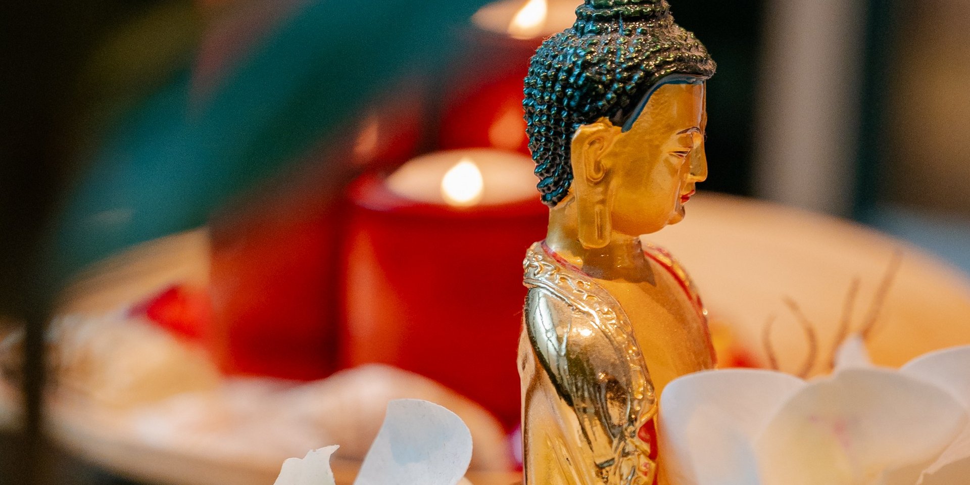 Eine kleine Buddha-Statue umgeben von brennenden roten Kerzen und weißen Orchideenblüten im Hotel Vier Jahreszeiten am Schluchsee.