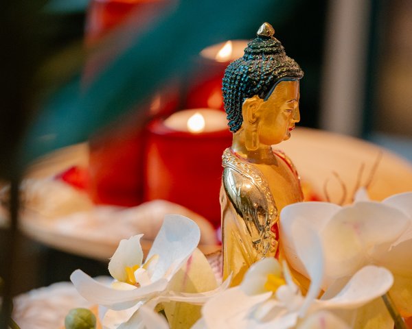 Eine kleine Buddha-Statue umgeben von brennenden roten Kerzen und weißen Orchideenblüten im Hotel Vier Jahreszeiten am Schluchsee.
