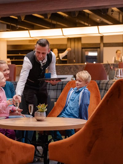 Kinder sitzen gespannt in den gemütlichen, orangen Sesseln der Lobby.