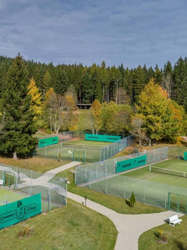 Außenansicht der gepflegten Tennis-Sandplätze des Hotels Vier Jahreszeiten am Schluchsee, umgeben von Schwarzwald-Panorama.