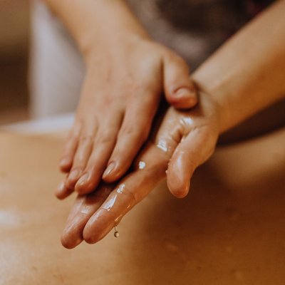 zwei Hände über einem Rücken, die Öl ineinander verstreichen 