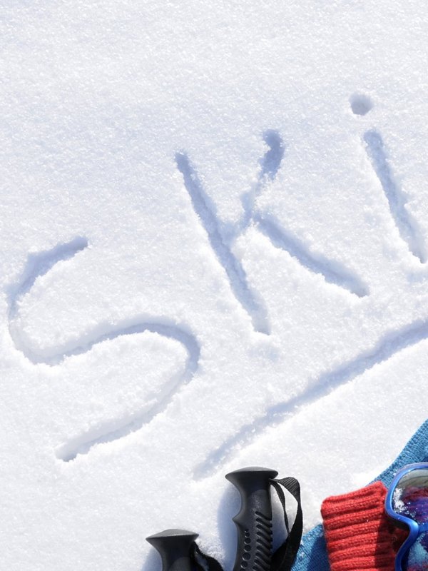 „SKI!“-Schriftzug in den Schnee geschrieben neben einer roten Skiausrüstung.