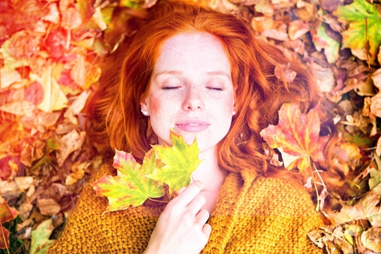 Frau liegt mit geschlossenen Augen im Herbstlaub