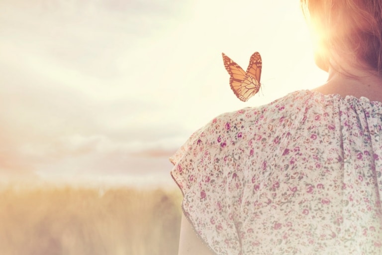 Frau blickt in den Sonnenuntergang während ein Schmetterling auf der Schulter sitzt