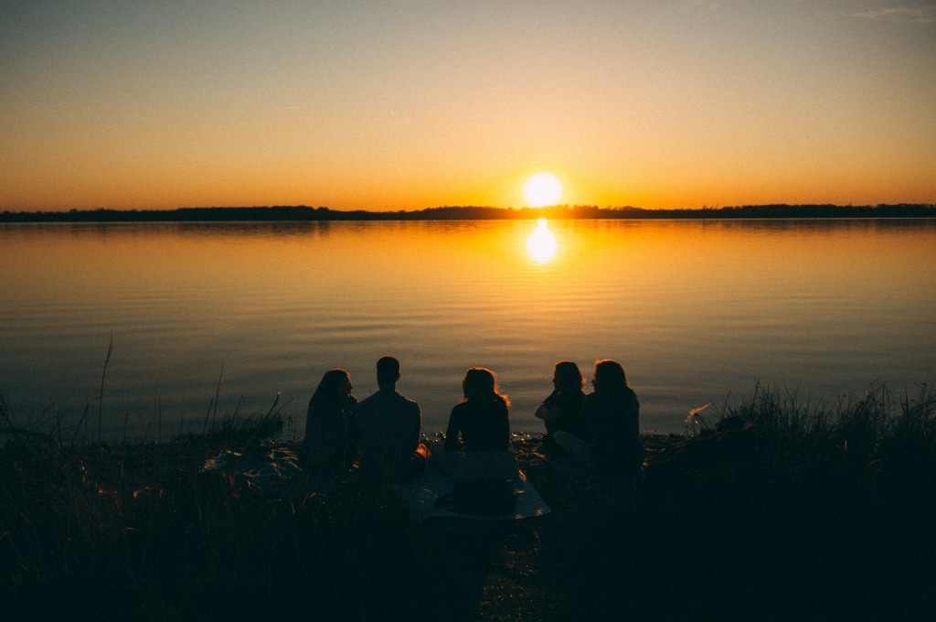 Gruppe sitzt am See und blickt auf Sonnenuntergang